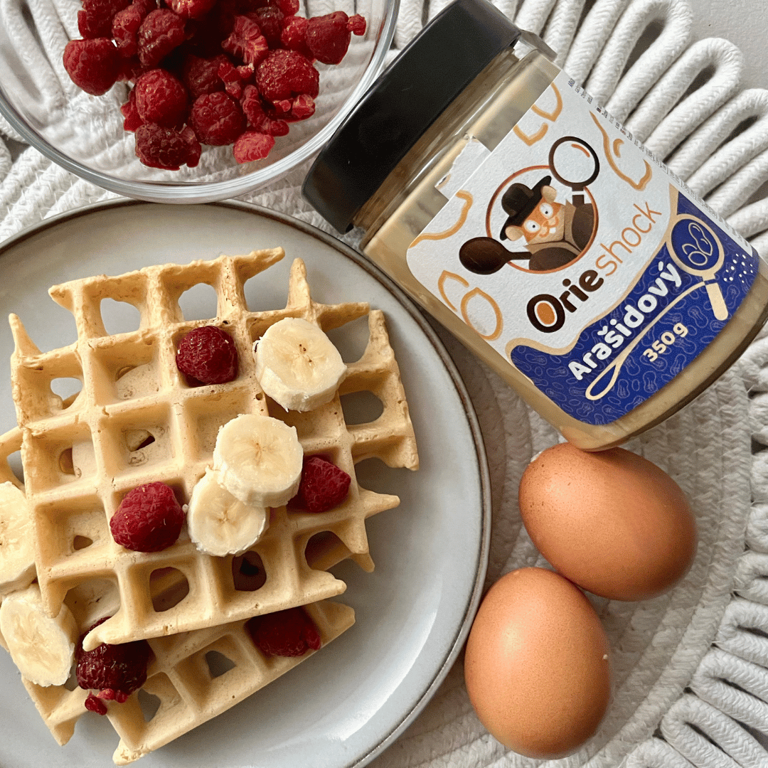Orieshock arašidový na ilustračnej fotografií k receptu na arašidové waffle len z 2 ingrediencií. Na stole je položený Orieshock 350g, hotové waffle a maliny.